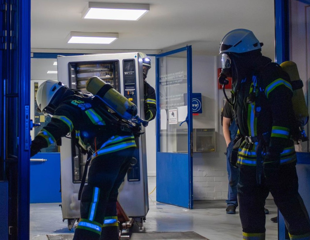 Nach einem Brand in einem Industriebetrieb in Einbeck am 9. August 2024 transportieren Feuerwehrleute den betroffenen Automaten aus dem Gebäude. Foto: Vincent Sömmer/Kreisfeuerwehr